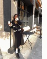 Woman wearing a black french aesthetic outfit, including a jacket and skirt, holding a coffee cup.