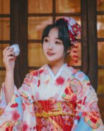 Woman wearing a pink new year kimono with floral details, holding a teacup.