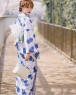 A woman wearing a blue japanese yukata with a floral pattern, set against a stone pathway.