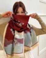 Woman wearing a maroon vegan cashmere scarf with floral pattern and beige fringe.