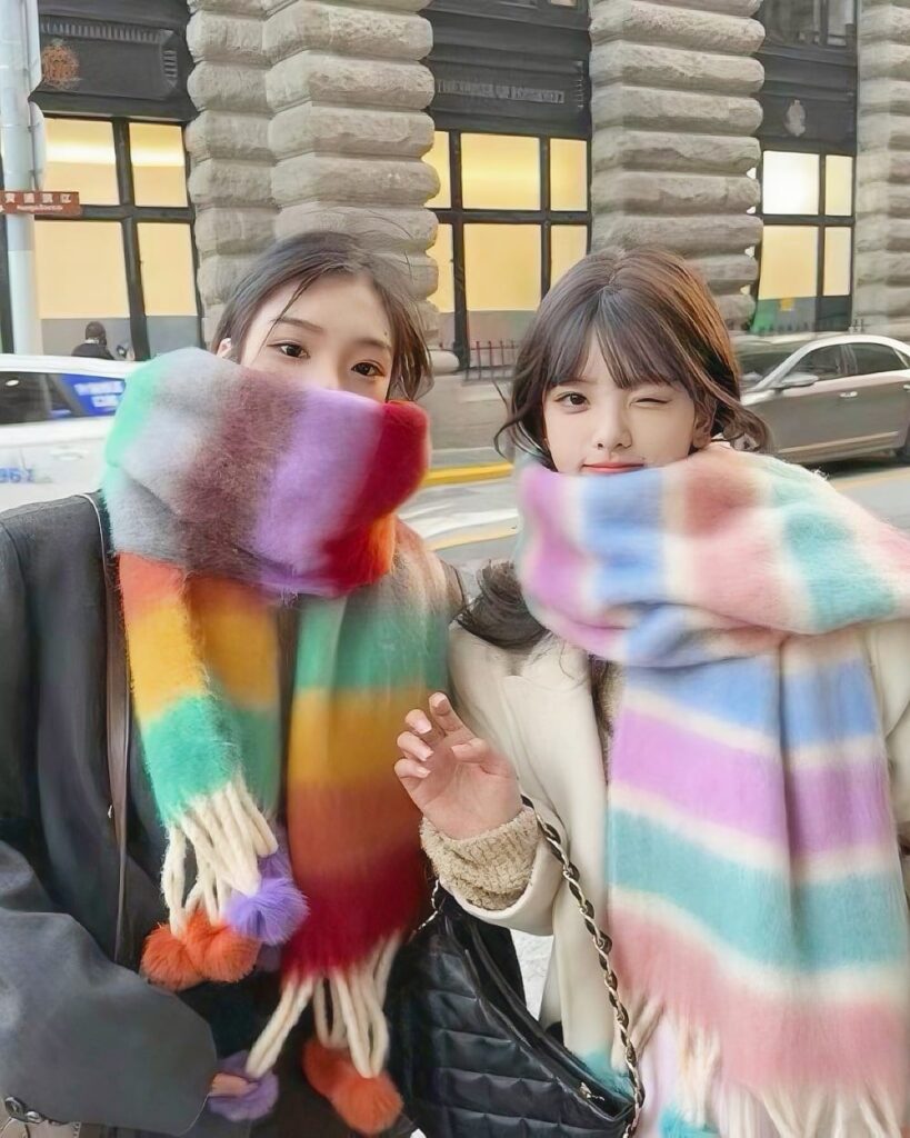 Two women wearing a fluffy kawaii rainbow scarf, vibrant colors, winter fashion.