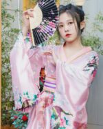 A woman wearing a pink short floral kimono with floral and bird patterns in Japanese aesthetic style.