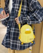 Yellow cartoon messenger bag with a duck design, held by a person.