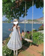 Woman wearing a lace bow long dress, cottagecore aesthetic dress, outdoors by a lake with a swing.