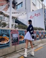 Woman wearing a black bowed pullover sweater, white dress, and thigh-high socks outdoors.