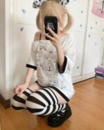 Close-up of a white harajuku kawaii t-shirt with cartoon designs and black striped leggings.