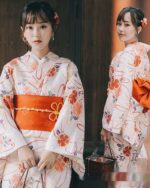 Two women wearing a white summer anime yukata with floral and orange patterns. It features a wide obi belt.