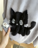 Close-up of a Black Neko Sweater featuring a plush black cat design with white details on a grey knit.