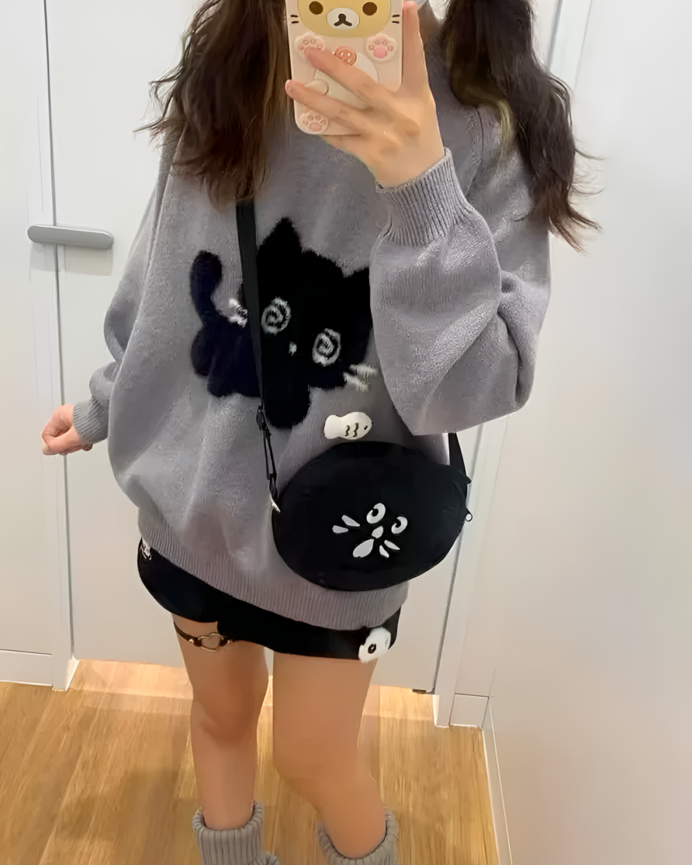 Woman wearing a Black Neko Sweater with a cat graphic and a crossbody bag.