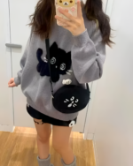 Woman wearing a Black Neko Sweater with a cat graphic and a crossbody bag.