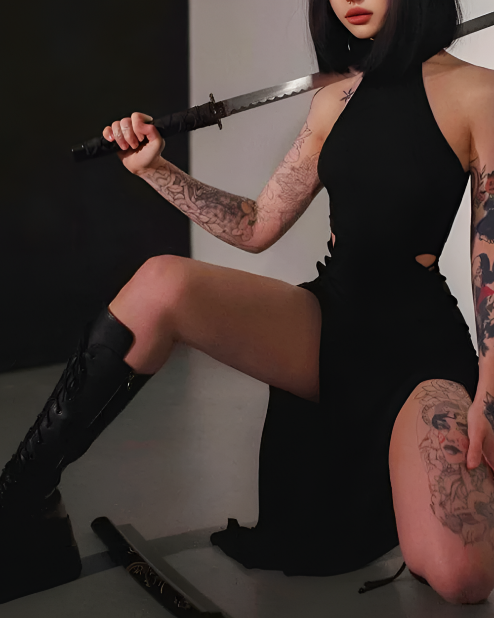 Model wearing a black Nu-Goth Aesthetic Dress, thigh-high boots, and holding a katana sword.