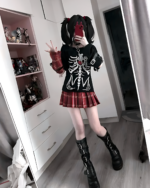 Model wearing the Needy Girl Overdose T-Shirt, featuring a skeleton print, with a plaid skirt and boots.