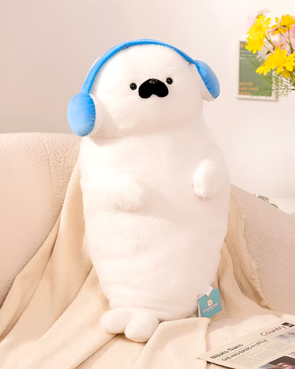 A white Kawaii Seal Plushie with blue headphones, sitting on a couch.
