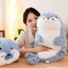 A gray Kawaii Seal Plushie is held by a young woman in a room setting.
