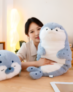 A gray Kawaii Seal Plushie is held by a young woman in a room setting.
