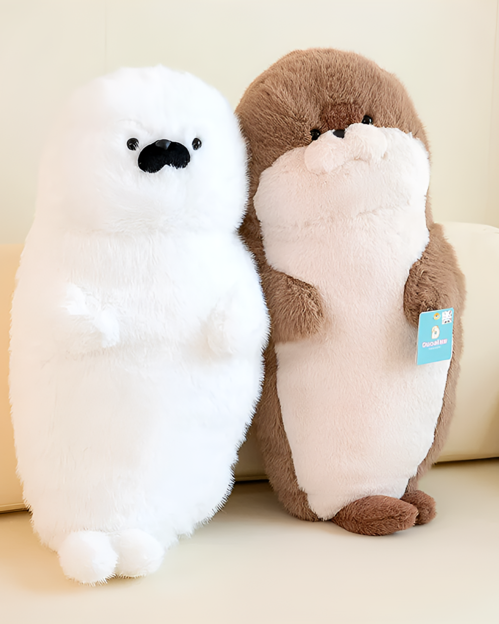 Two Kawaii Seal Plushies, a white seal and a brown otter, displayed on a sofa.
