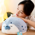 A Kawaii Seal Plushie, a soft, grey stuffed animal held by a person.