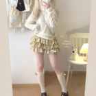 Model wearing a beige, ruffled mini skirt – Yume Kawaii Aesthetic outfit with a cream sweater and socks.