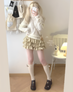 Model wearing a beige, ruffled mini skirt – Yume Kawaii Aesthetic outfit with a cream sweater and socks.