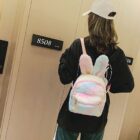 A pink Rabbit Ears Plush Backpack is worn by a person. It features soft plush material and rabbit ears.