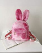 Pink Rabbit Ears Plush Backpack on a table with a book.