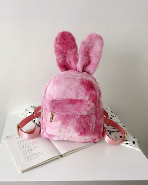 Pink Rabbit Ears Plush Backpack on a table with a book.