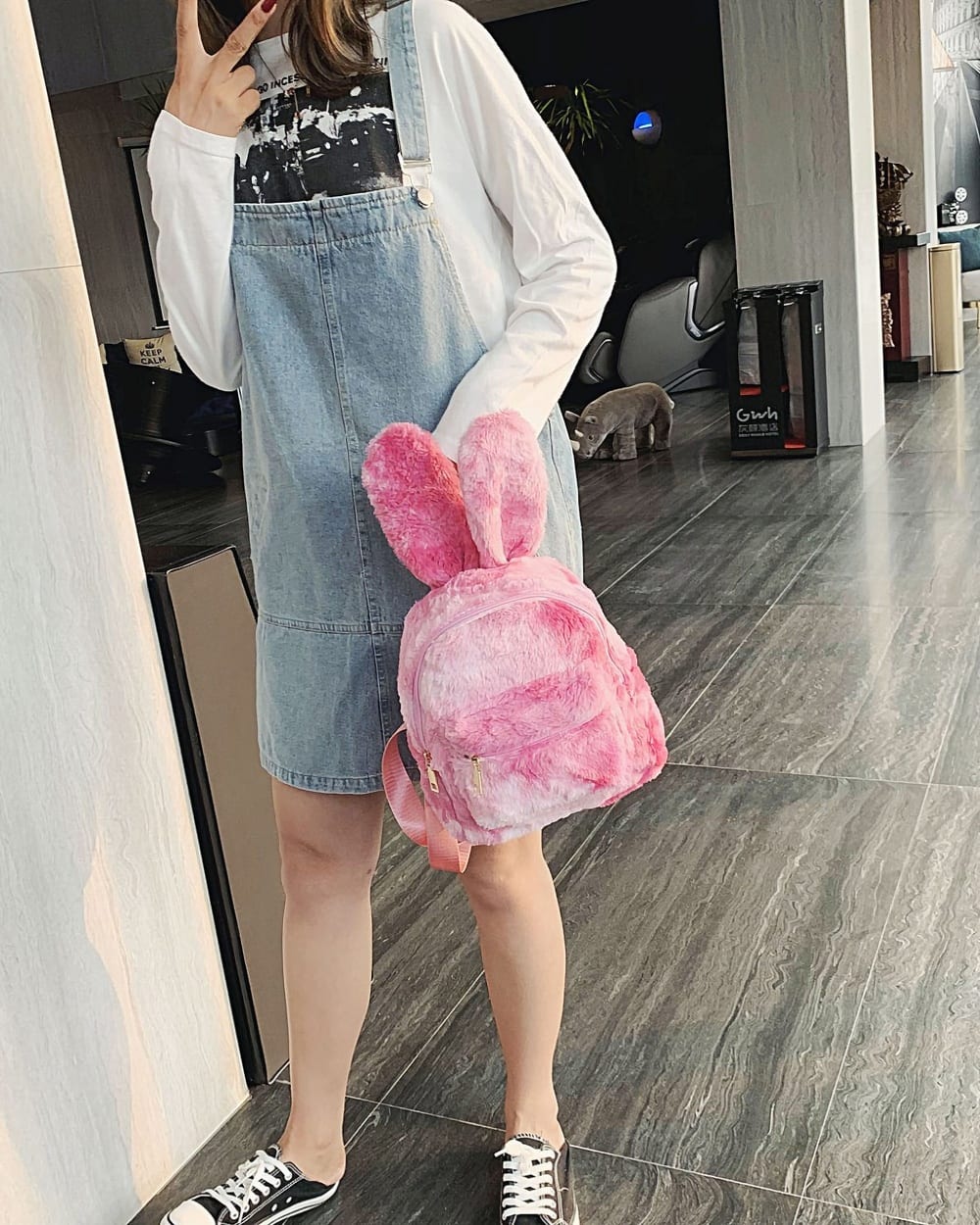 Pink Rabbit Ears Plush Backpack held by a person in a mall setting.