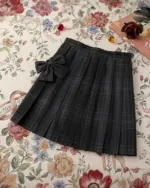 A black JK Plaid Skirt with a bow, displayed on a floral background.