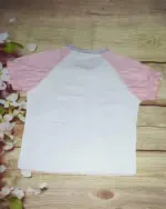 White Sugarbunnies T-Shirt with pink sleeves, on wooden background.