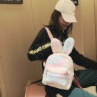 A pink and white Rabbit Ears Plush Backpack is worn by a woman.