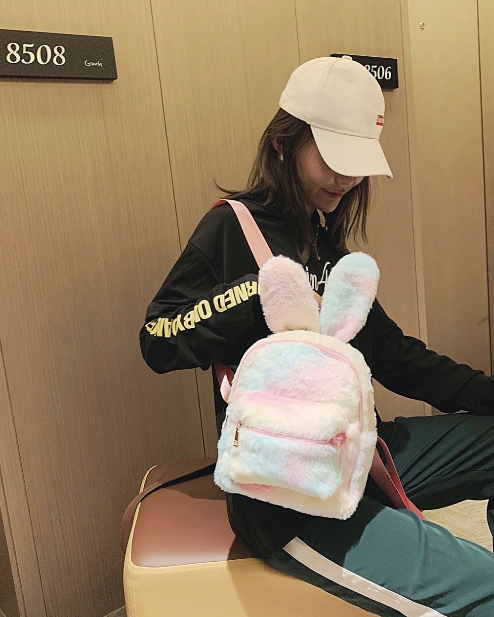 A pink and white Rabbit Ears Plush Backpack is worn by a woman.