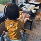 Child wearing a Jojifuku Hoodie enjoys a meal with plush toys.