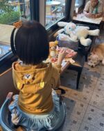 Child wearing a Jojifuku Hoodie enjoys a meal with plush toys.