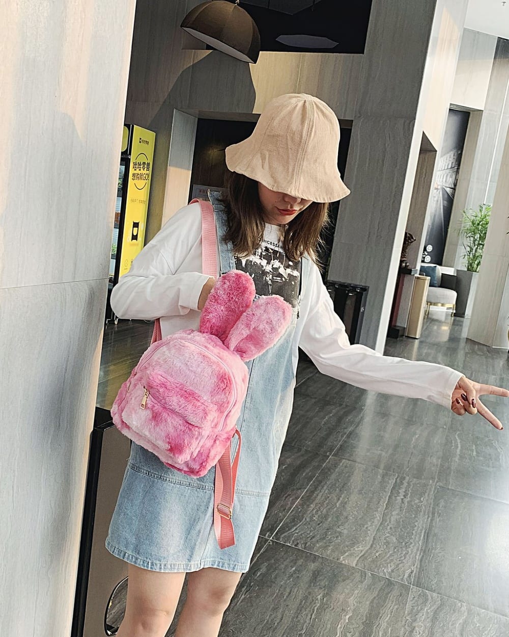 A pink Rabbit Ears Plush Backpack is carried by a person in a casual outfit.