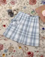 A light blue and white JK Plaid Skirt with a tie detail, displayed on a patterned rug.