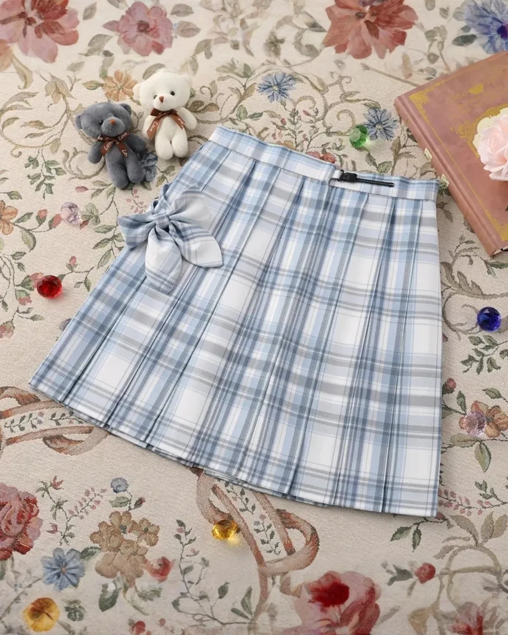 A light blue and white JK Plaid Skirt with a tie detail, displayed on a patterned rug.