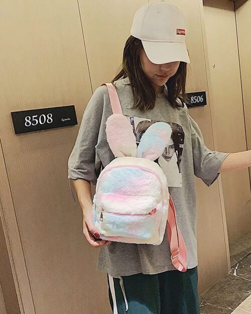 A pink Rabbit Ears Plush Backpack being carried by a person.
