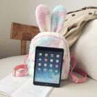 Colorful Rabbit Ears Plush Backpack displayed with an iPad on a table.