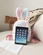 Colorful Rabbit Ears Plush Backpack displayed with an iPad on a table.