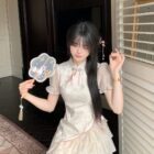 A woman wearing a layered, ruffled Qi Lolita Dress in a light beige color, holding a fan.