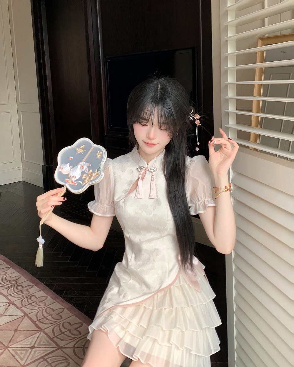 A woman wearing a layered, ruffled Qi Lolita Dress in a light beige color, holding a fan.