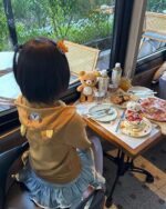 Woman wearing a Jojifuku Hoodie enjoying a brunch with teddy bears and a cake.