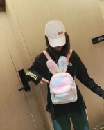 A pink and white Rabbit Ears Plush Backpack is worn by a person.