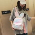 A pink and white Rabbit Ears Plush Backpack is worn by a person in a public space.