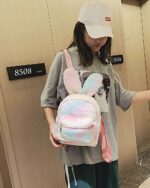 A pink and white Rabbit Ears Plush Backpack is worn by a person in a public space.