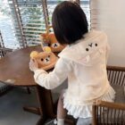 Person wearing a white Jojifuku Hoodie with ear details, holding a plush bear.