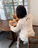 Person wearing a white Jojifuku Hoodie with ear details, holding a plush bear.