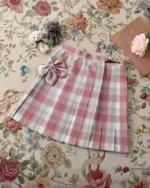 Pink JK Plaid Skirt with bow, displayed on a floral background.