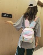 A pink and white Rabbit Ears Plush Backpack worn by a person.