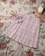 Pink JK Plaid Skirt with bow detail on a floral rug background.